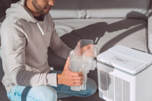 Man replacing the water container in a dehumidifier, demonstrating routine maintenance essential for managing indoor air humidity in New Orleans homes.