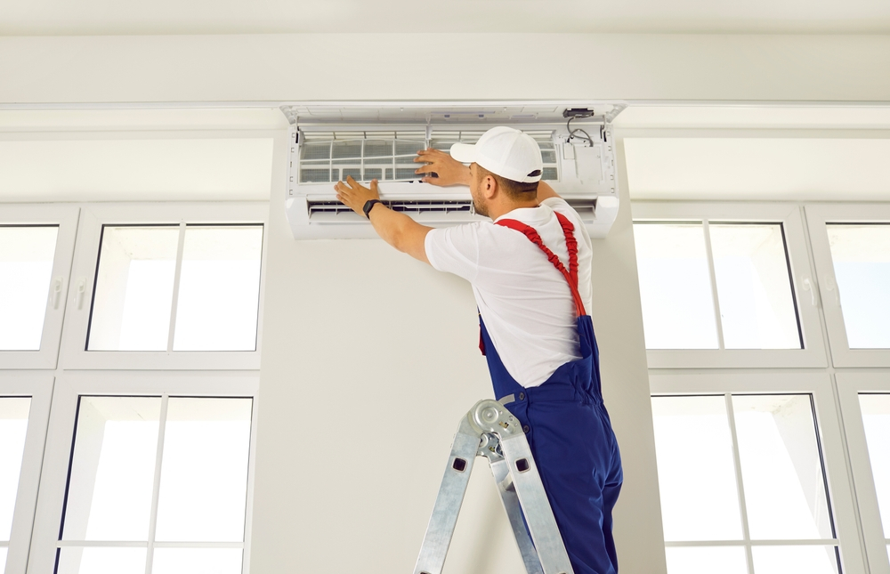 Worker installs ventilation system in office from ladder. Doing some maintenance to an air conditioner system in the living room.