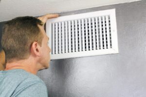 HVAC technician in New Orleans assessing the cleanliness and functionality of a residential air vent and duct system.